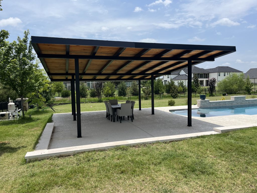 Steel frame patio structure with wooden ceiling built by Texas IE Solar Roofing and Construction in Parker, TX — free standing structure over patio dining set and next to pool.